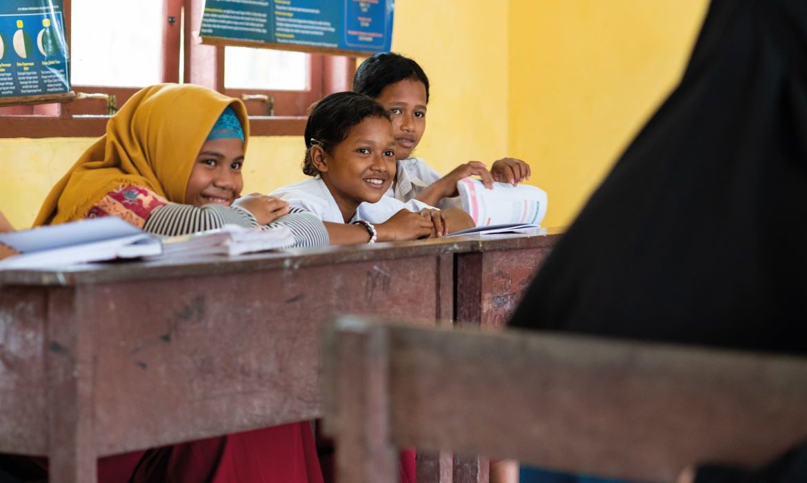 children sit at a school desk smiling