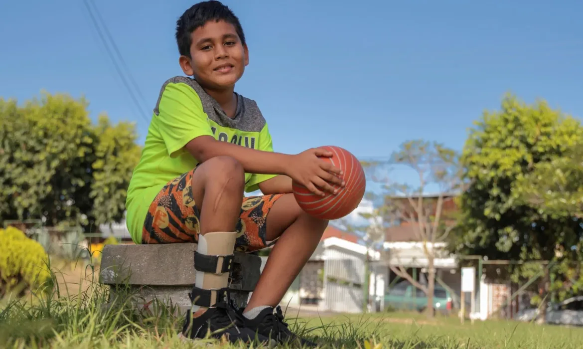 a boy sitting down and smiling at the camera whilst holding a ball